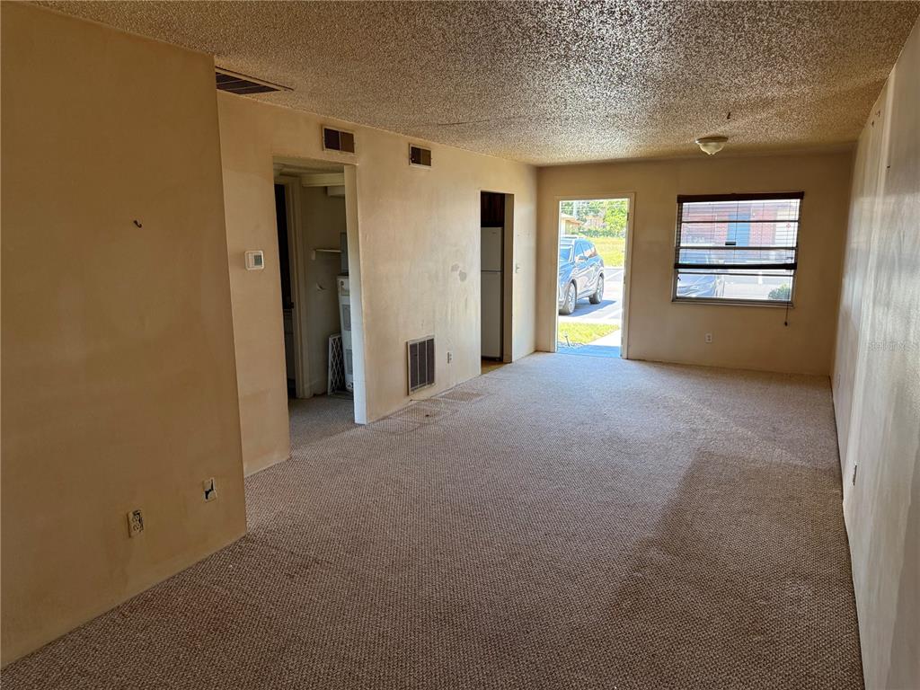 An empty living room features beige carpet, textured ceilings, and a doorway leading outside — 24862 US HIGHWAY 19 N UNIT 2803, CLEARWATER, FL