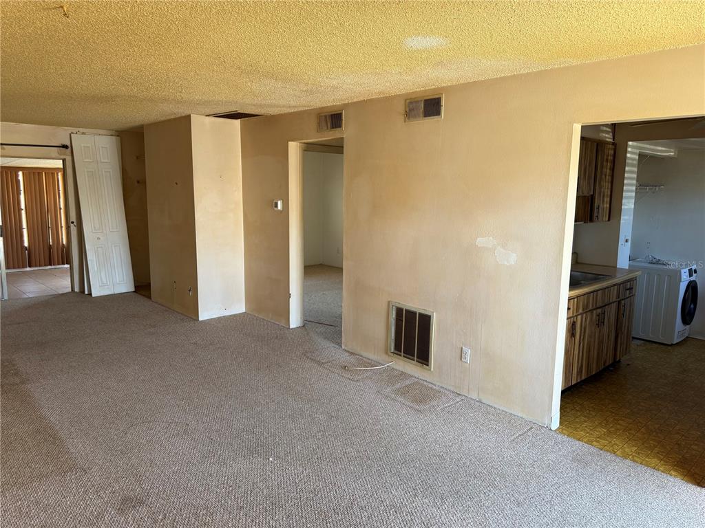 A carpeted living room leads to a kitchen and a hallway in a residential interior — 24862 US HIGHWAY 19 N UNIT 2803, CLEARWATER, FL