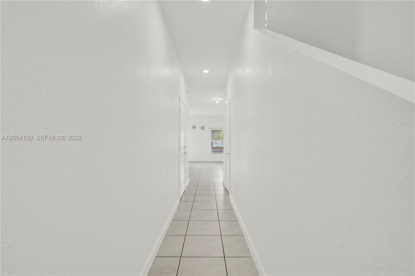 A narrow hallway with white walls and light-colored tile flooring leads toward a window — 1161 SW 8th Ave, Florida City FL 33034, FLORIDA CITY, FL