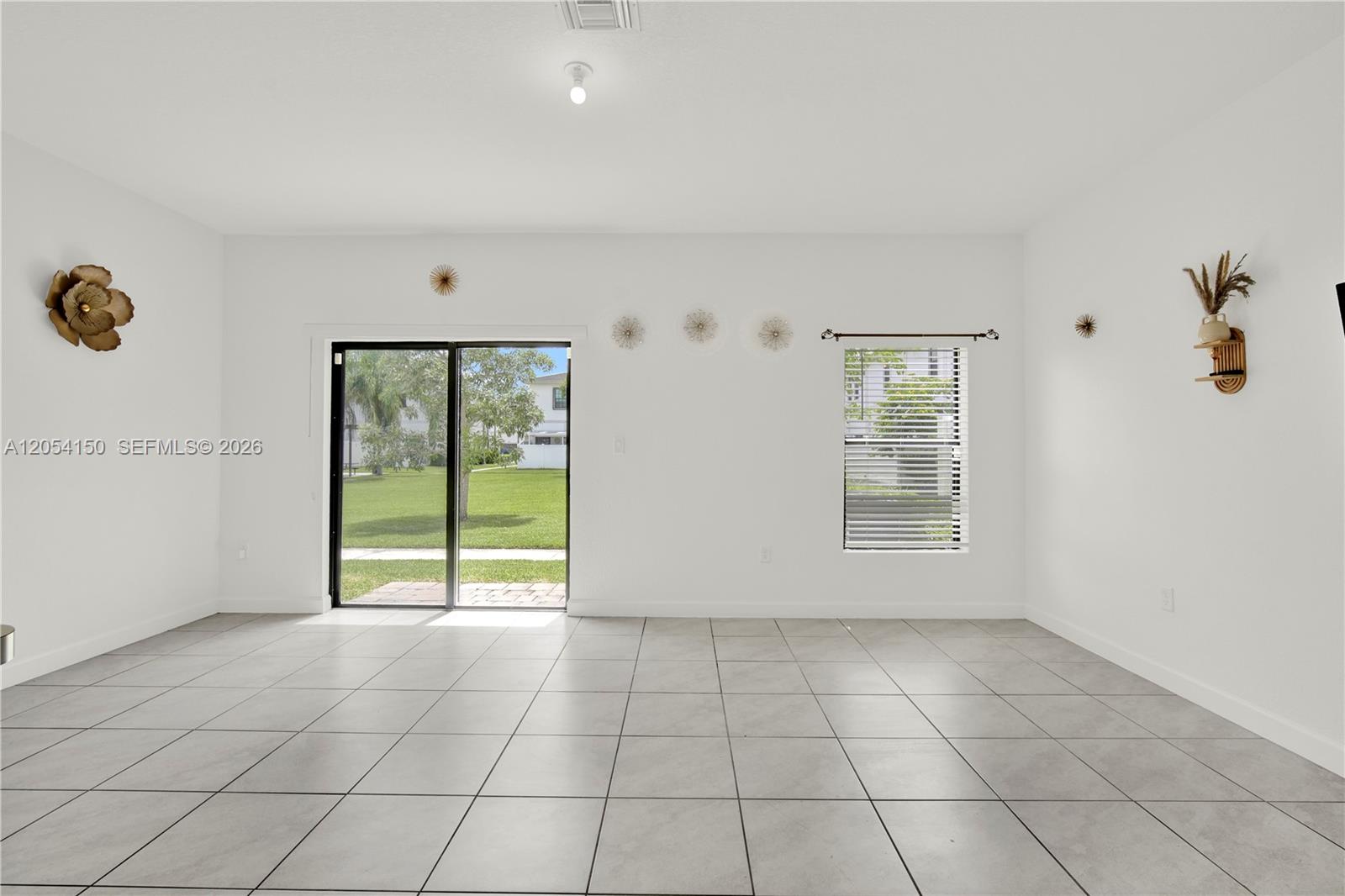 A bright, empty living room features white walls, large light-colored floor tiles, and a sliding door — 1161 SW 8th Ave, Florida City FL 33034, FLORIDA CITY, FL