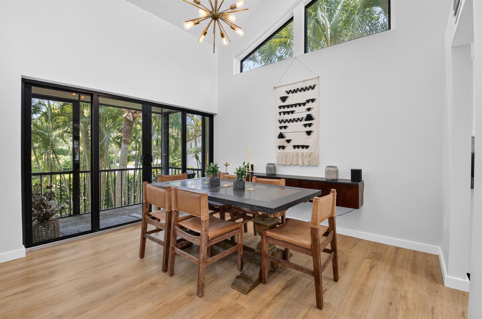 A dining room features a dark table, leather chairs, a chandelier, and large sliding glass doors — 6760 Willow Wood Drive # 1206, Boca Raton FL 33434, BOCA RATON, FL