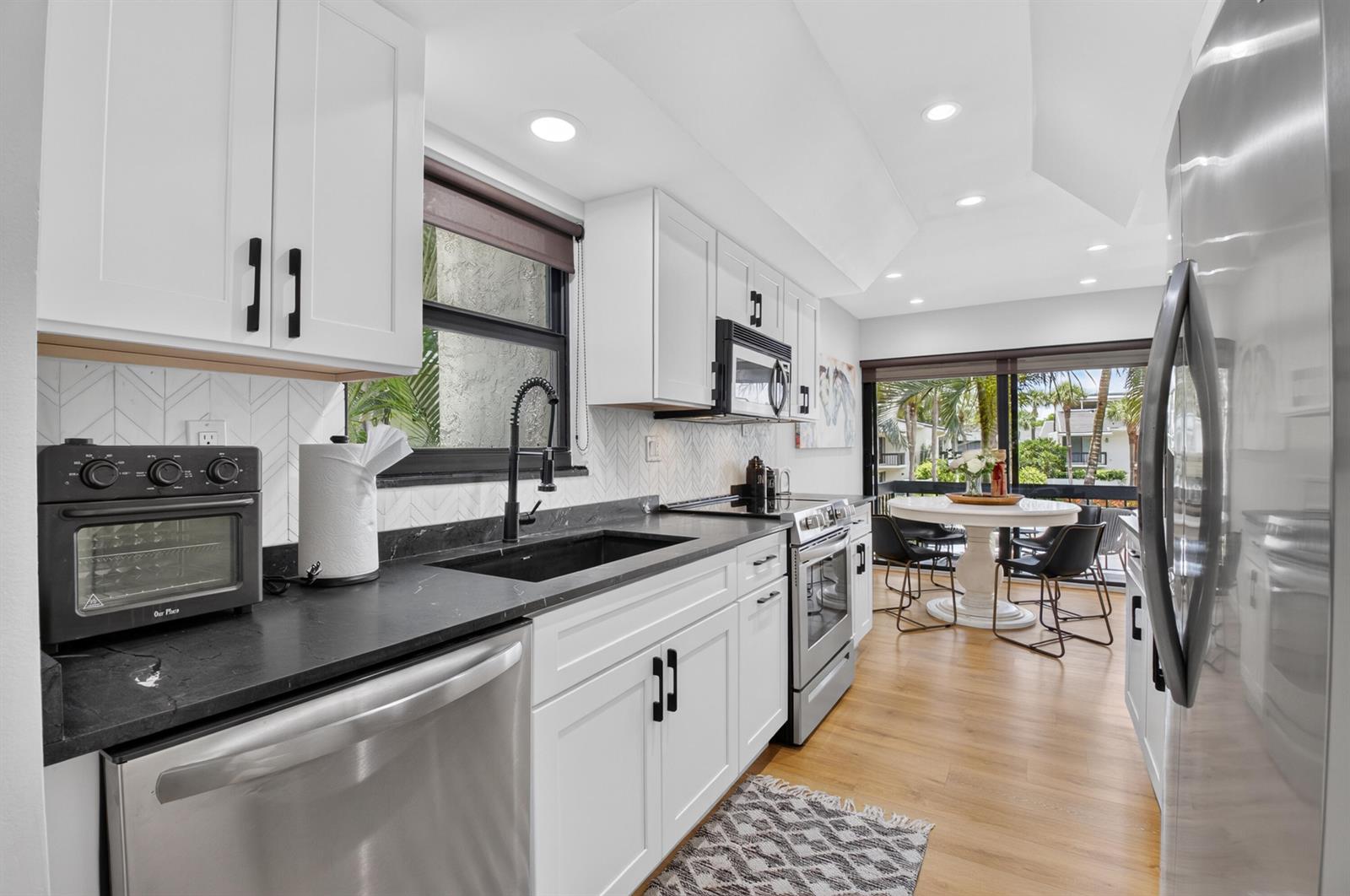 A modern kitchen features white cabinets, black countertops, stainless steel appliances, and a dining area — 6760 Willow Wood Drive # 1206, Boca Raton FL 33434, BOCA RATON, FL