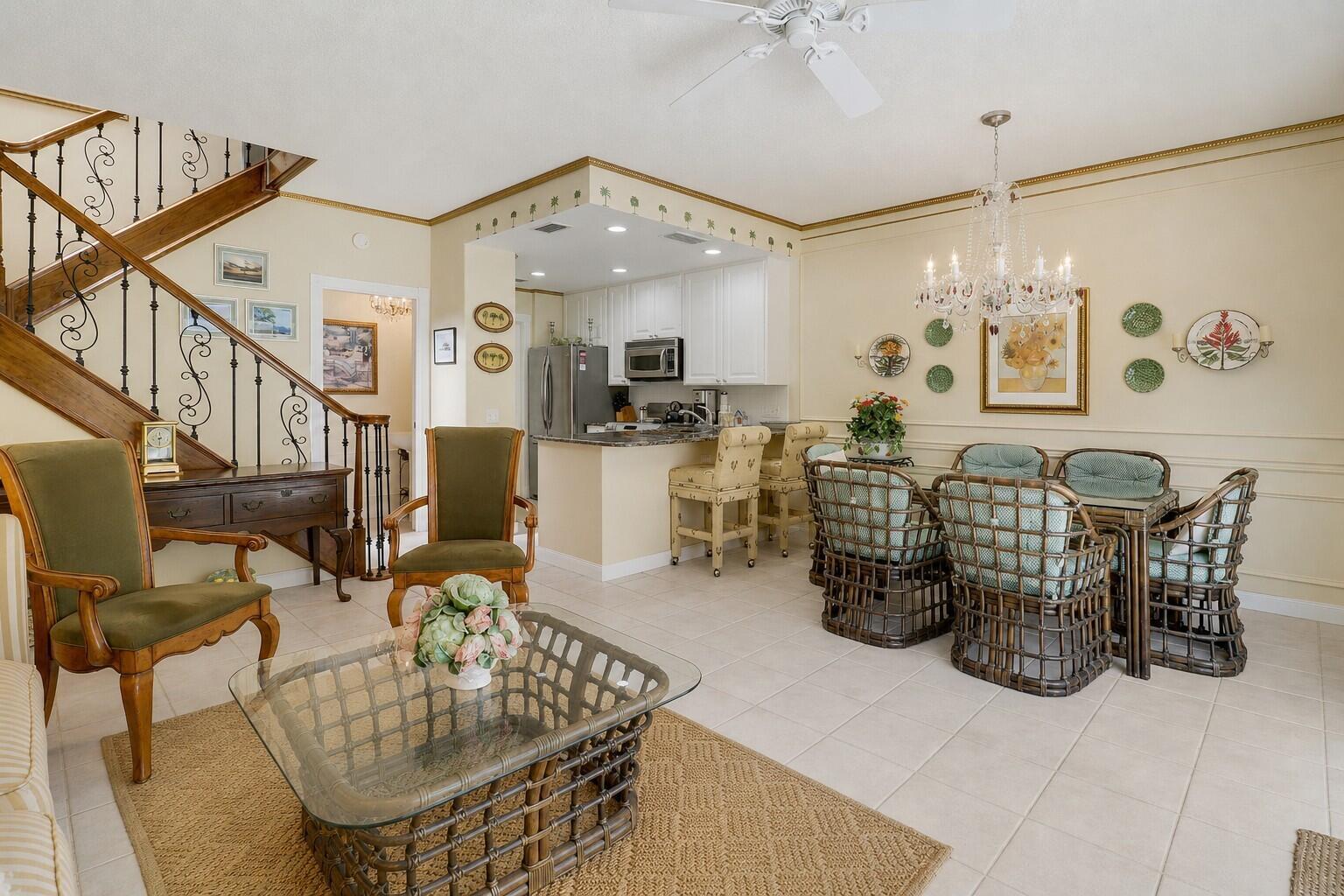 An open-concept living and dining area features a staircase, kitchen island, and rattan furniture — 77 Laurel Oaks Circle, Tequesta FL 33469, TEQUESTA, FL