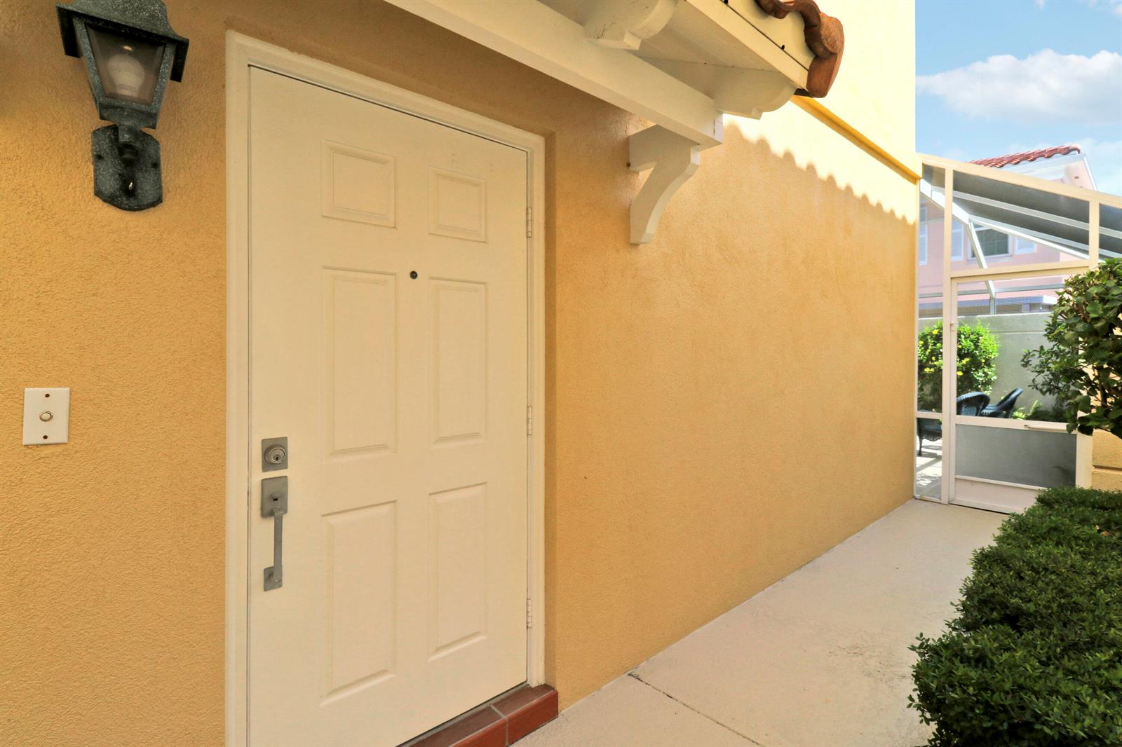 A white front door with a handle set sits on a yellow stucco exterior wall — 77 Laurel Oaks Circle, Tequesta FL 33469, TEQUESTA, FL