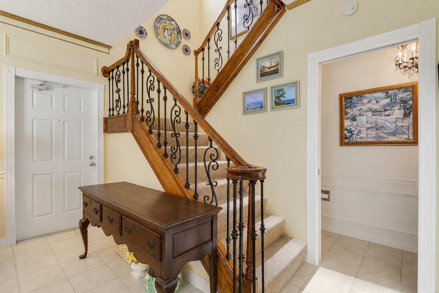 An entryway features a wooden staircase with iron railings, a console table, and wall decor — 77 Laurel Oaks Circle, Tequesta FL 33469, TEQUESTA, FL