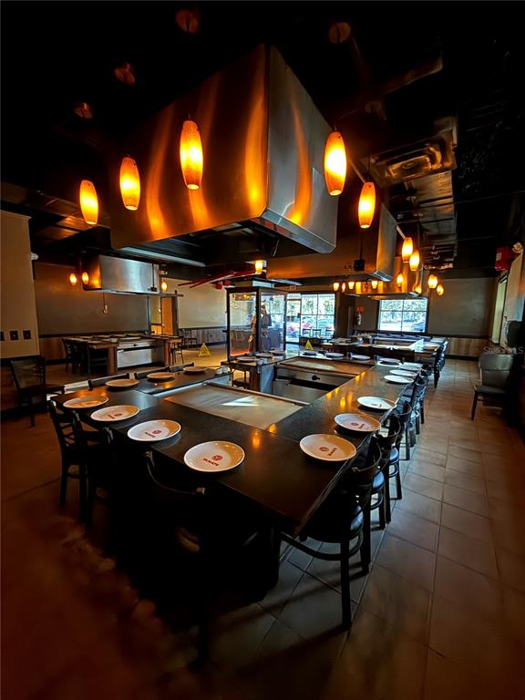 A restaurant dining room features multiple hibachi grill tables with overhead ventilation hoods and pendant lighting — 526 NW 60TH STREET, GAINESVILLE, FL