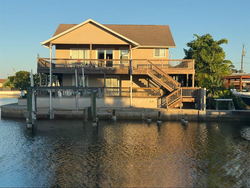 A two-story waterfront house with a large wooden deck and staircase overlooking a canal — 13825 SAN JUAN AVENUE, HUDSON, FL