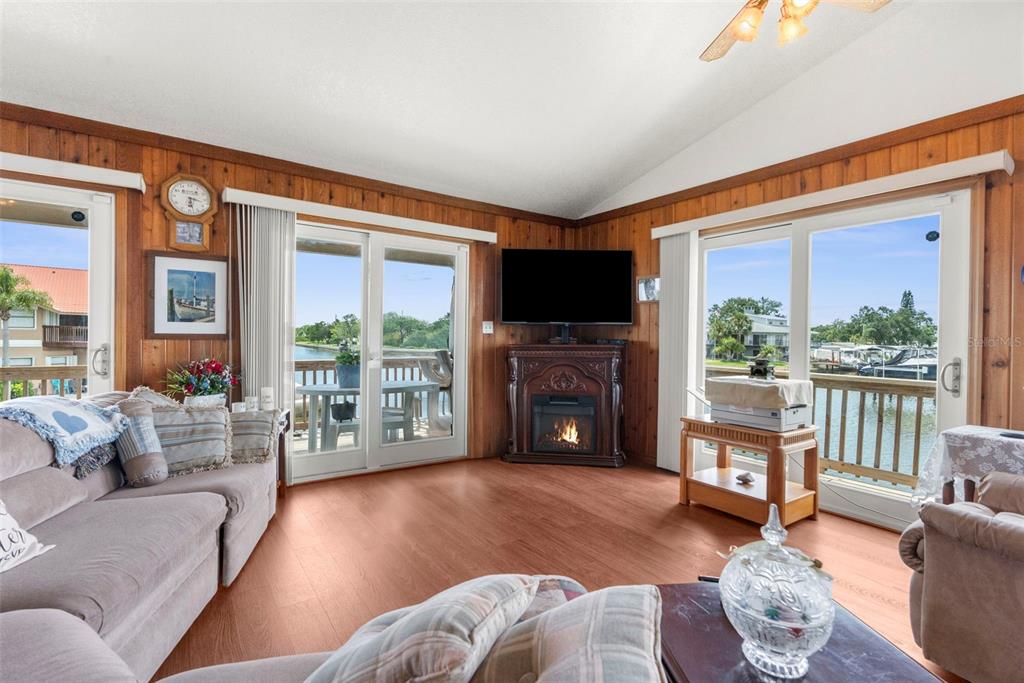A living room with wood-paneled walls, a corner fireplace, and sliding glass doors overlooking water — 13825 SAN JUAN AVENUE, HUDSON, FL