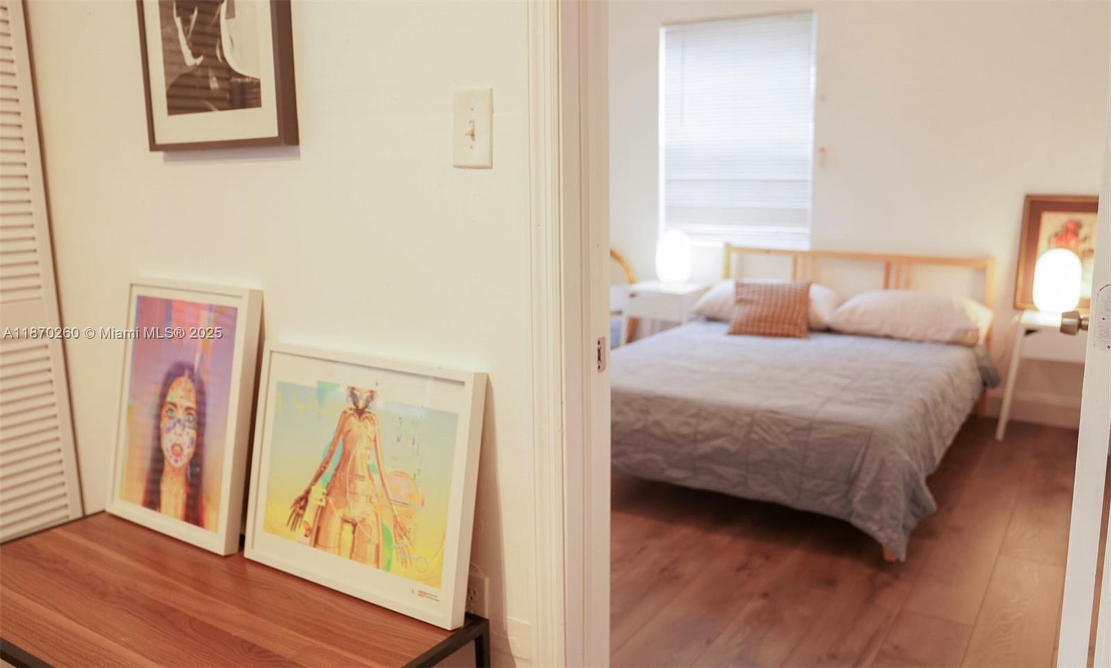 A hallway with framed artwork leads into a bedroom featuring a bed and wood flooring — 68 NW 45th St # 2, Miami FL 33127, MIAMI, FL