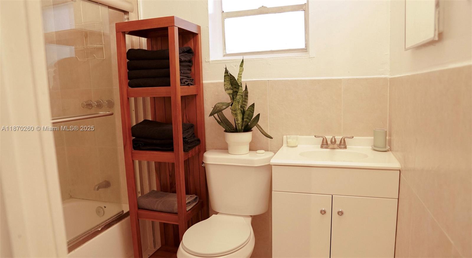 A bathroom features a wooden shelving unit, a toilet, a vanity, and a shower-tub combination — 68 NW 45th St # 2, Miami FL 33127, MIAMI, FL