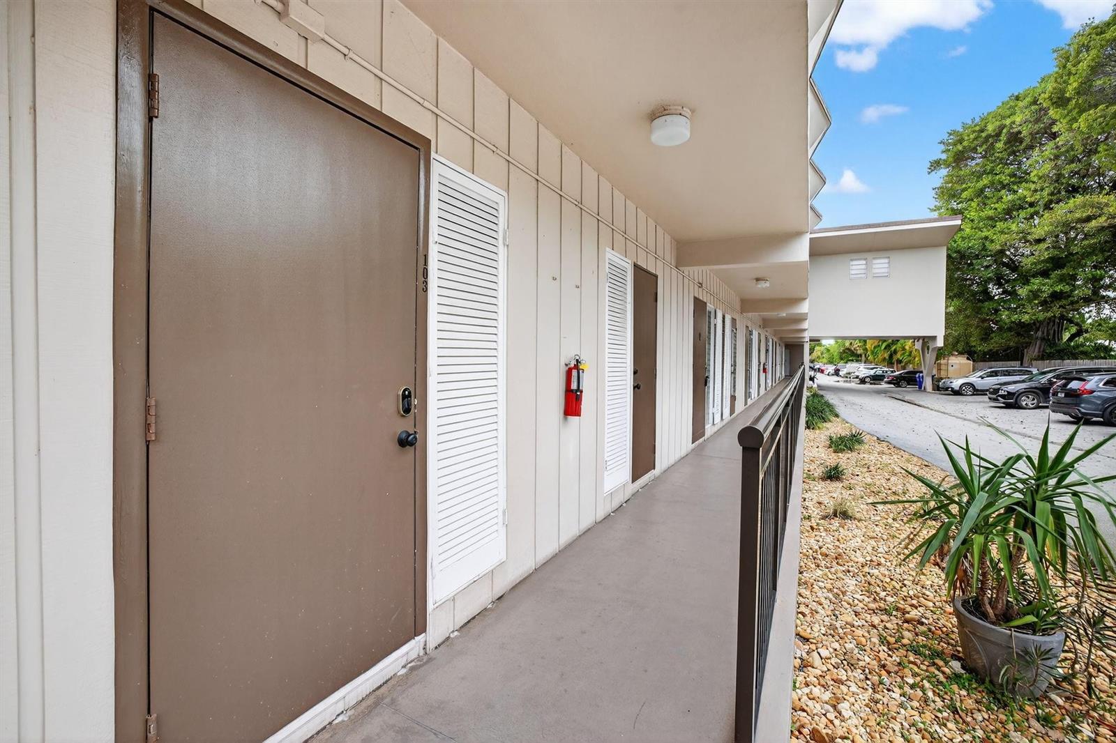 An exterior walkway features brown doors, a fire extinguisher, and a metal railing — 1967 S Ocean Boulevard # 103, Pompano Beach FL 33062, POMPANO BEACH, FL