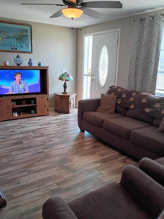 A living room features wood-look tile flooring, a brown sofa, and a television console — 7534 ROTTINGHAM ROAD, PORT RICHEY, FL