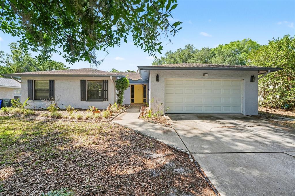 A single-story house with a white stucco exterior, a yellow front door, and a garage — 851 ROLLING WOODS LANE, LAKELAND, FL