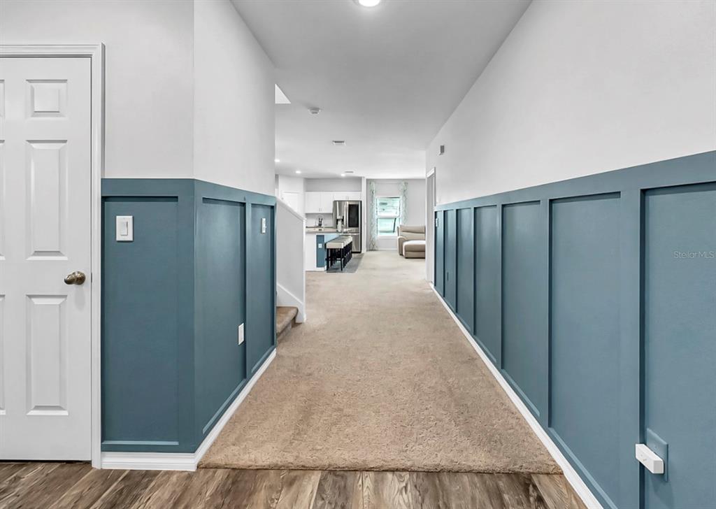 A hallway with blue board and batten wainscoting leads to an open-concept kitchen and living area — 13108 SHUMARD WAY, RIVERVIEW, FL