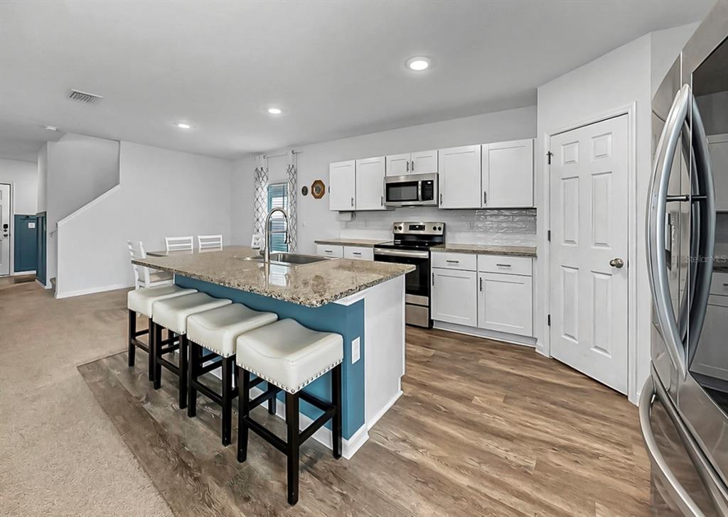 A kitchen features white cabinets, a granite-topped island with four stools, and wood-look flooring — 13108 SHUMARD WAY, RIVERVIEW, FL