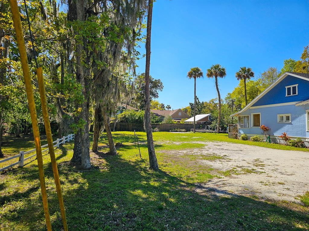 A large, grassy backyard with mature trees and a blue house on the right — 820 CANAL STREET, NEW SMYRNA BEACH, FL