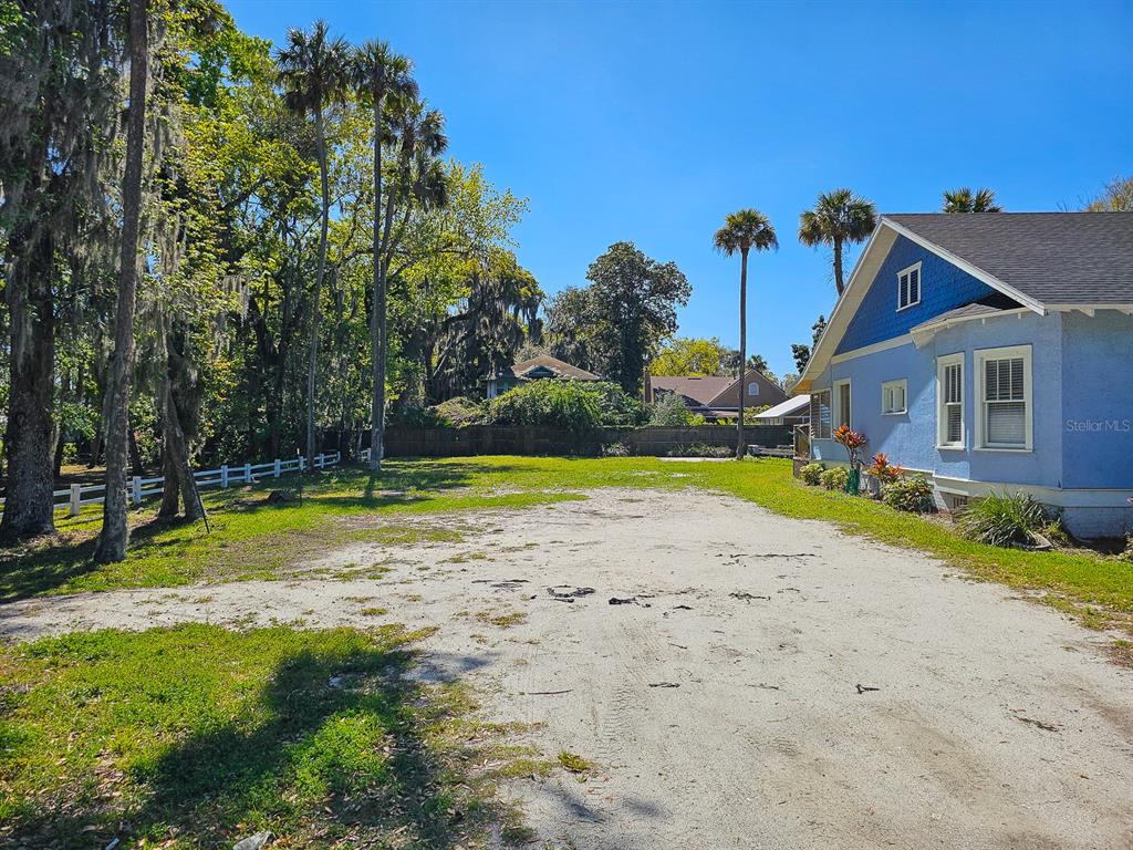 A blue house sits beside a large, unpaved dirt lot with trees and a fence — 820 CANAL STREET, NEW SMYRNA BEACH, FL