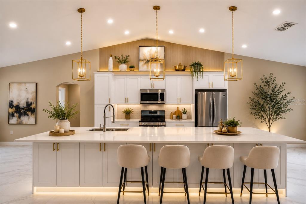 A modern kitchen features white cabinetry, a large quartz island, and gold pendant lighting — 12783 LINDEN DRIVE, SPRING HILL, FL
