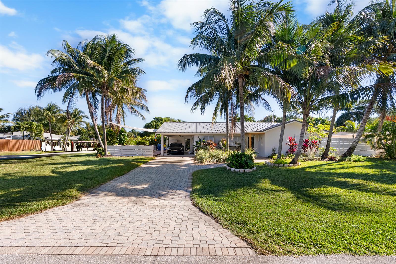 A single-story house with a metal roof and a paved driveway sits among palm trees — 1605 Treemont Avenue, Jupiter FL 33469, JUPITER, FL