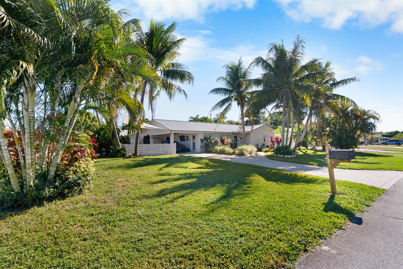 A single-story house with a metal roof and palm trees sits behind a grassy lawn — 1605 Treemont Avenue, Jupiter FL 33469, JUPITER, FL