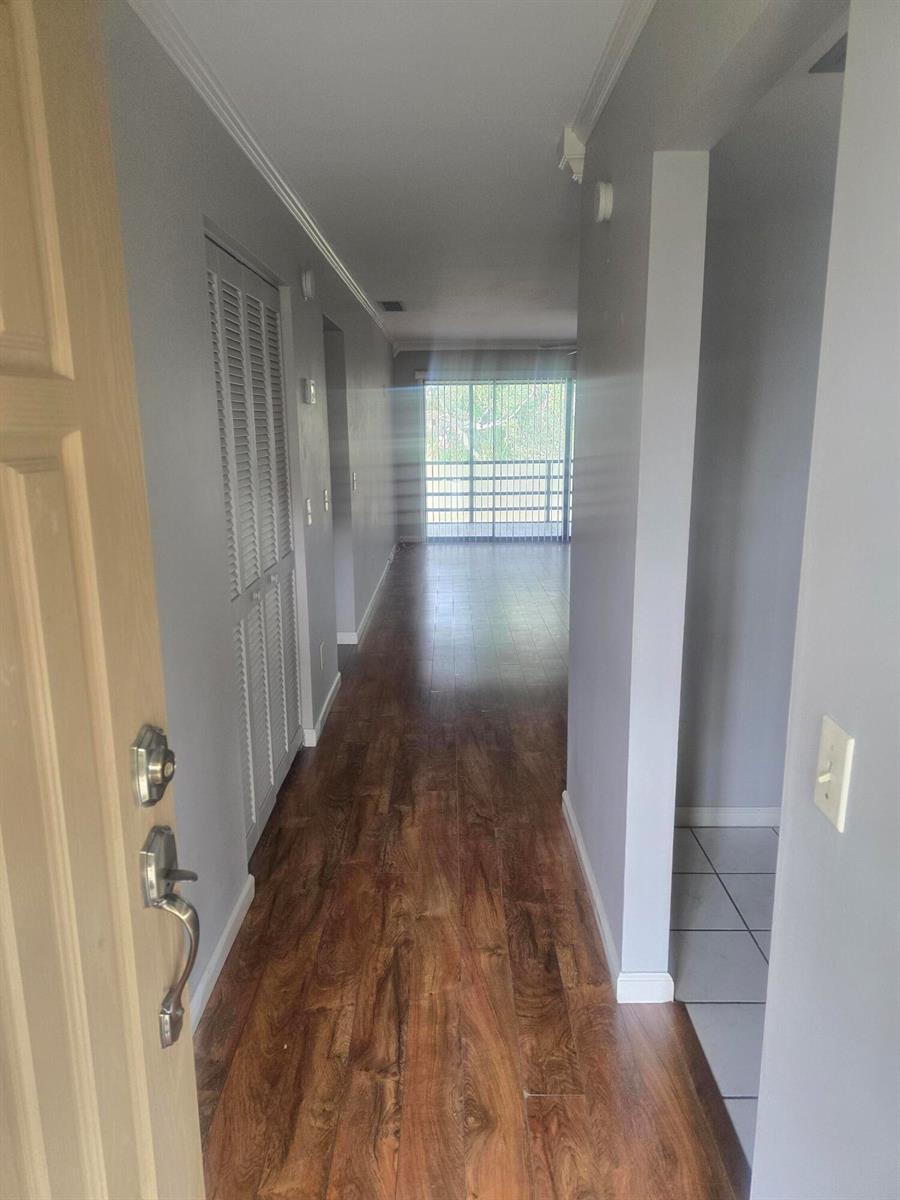 A hallway with wood-look flooring leads toward a sliding glass door with a balcony view — 400 18th Street # 5, Vero Beach FL 32960, VERO BEACH, FL