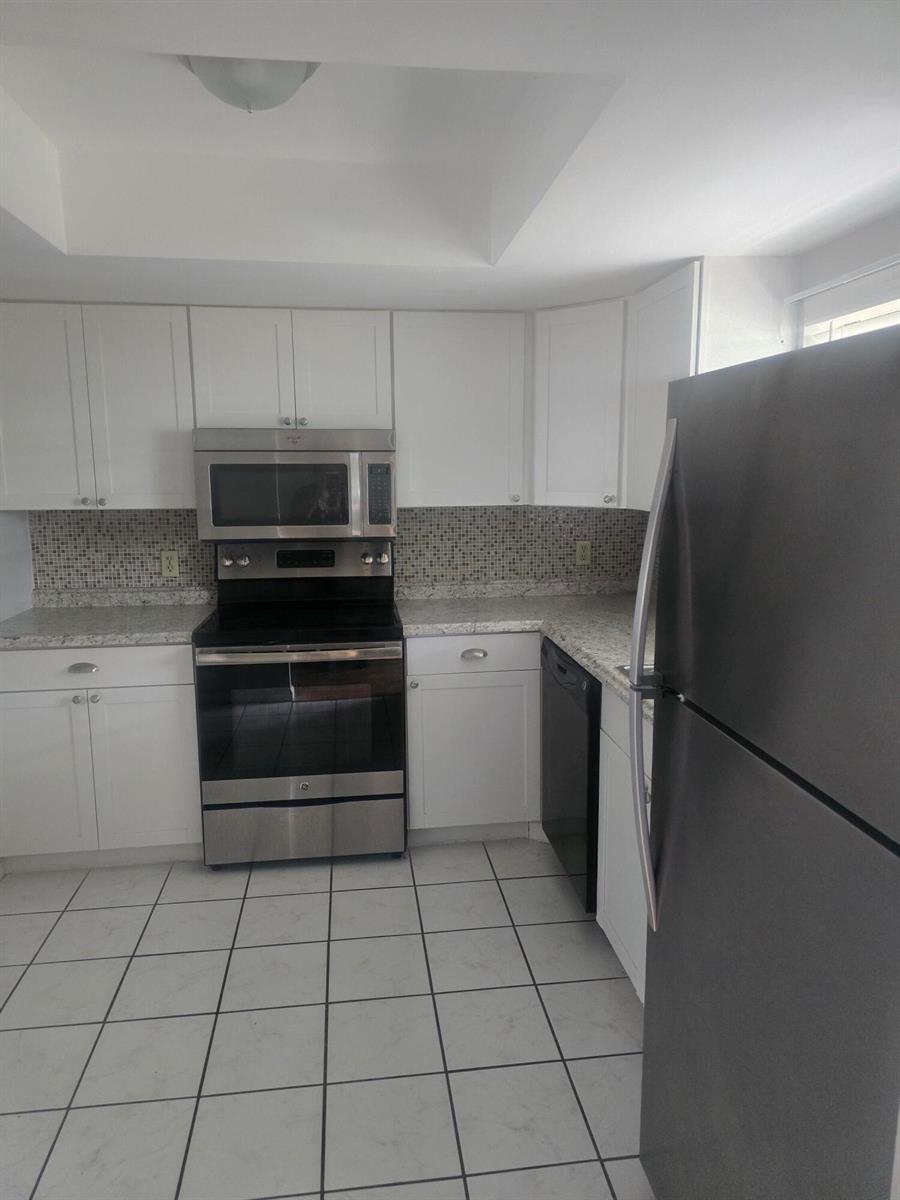 A kitchen features white cabinets, stainless steel appliances, a mosaic backsplash, and white tile flooring — 400 18th Street # 5, Vero Beach FL 32960, VERO BEACH, FL