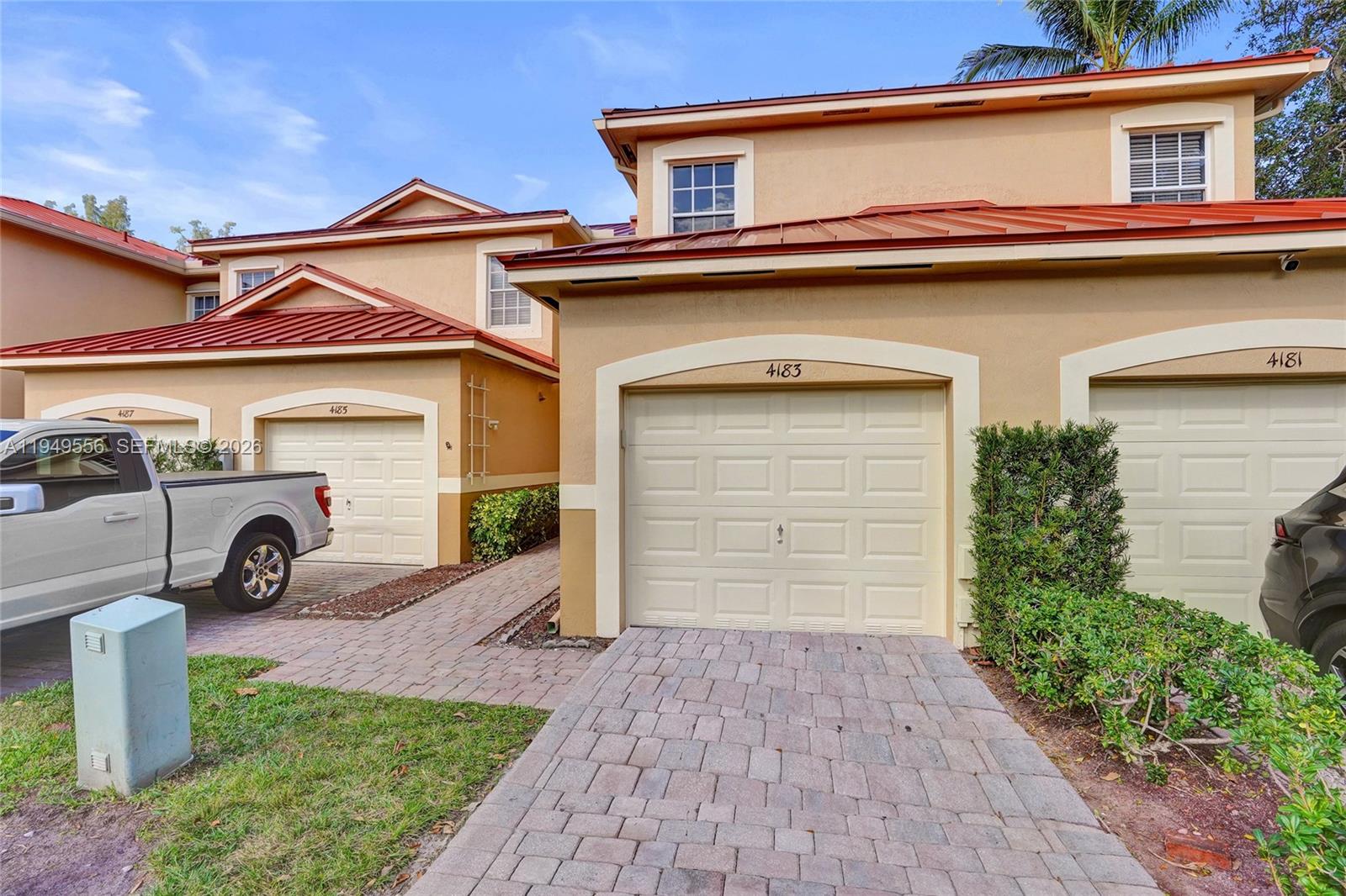 A row of tan townhomes features red metal roofs, paved driveways, and white garage doors — 4183 Crystal Lake Dr, Deerfield Beach FL 33064, DEERFIELD BEACH, FL