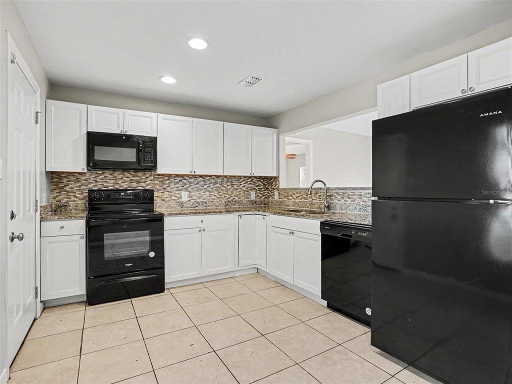 A kitchen features white cabinets, black appliances, granite countertops, and a tiled backsplash — 455 CART COURT, KISSIMMEE, FL