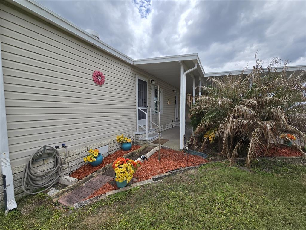 The exterior of a mobile home features light siding, a covered porch, and landscaping — 4122 GREENBLUFF ROAD UNIT 821, ZELLWOOD, FL