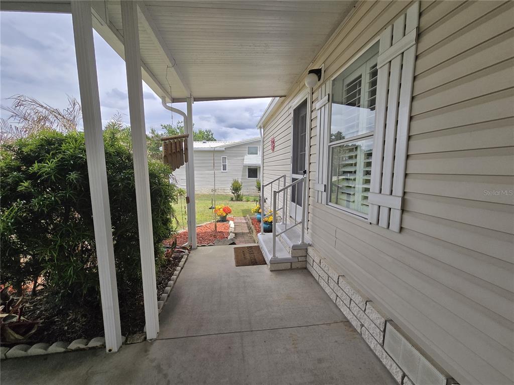 A covered concrete porch leads to the front entrance of a light-colored mobile home — 4122 GREENBLUFF ROAD UNIT 821, ZELLWOOD, FL