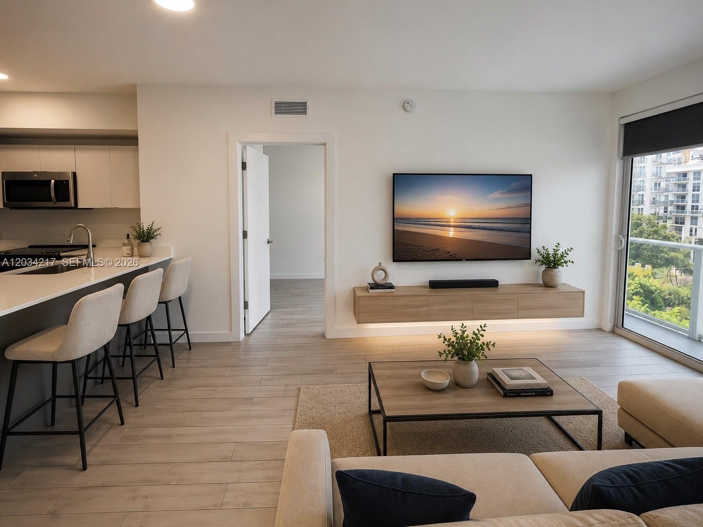 A modern living room features a floating media console, wall-mounted television, and an adjacent kitchen — 321 NE 26th St # 512, Miami FL 33137, MIAMI, FL