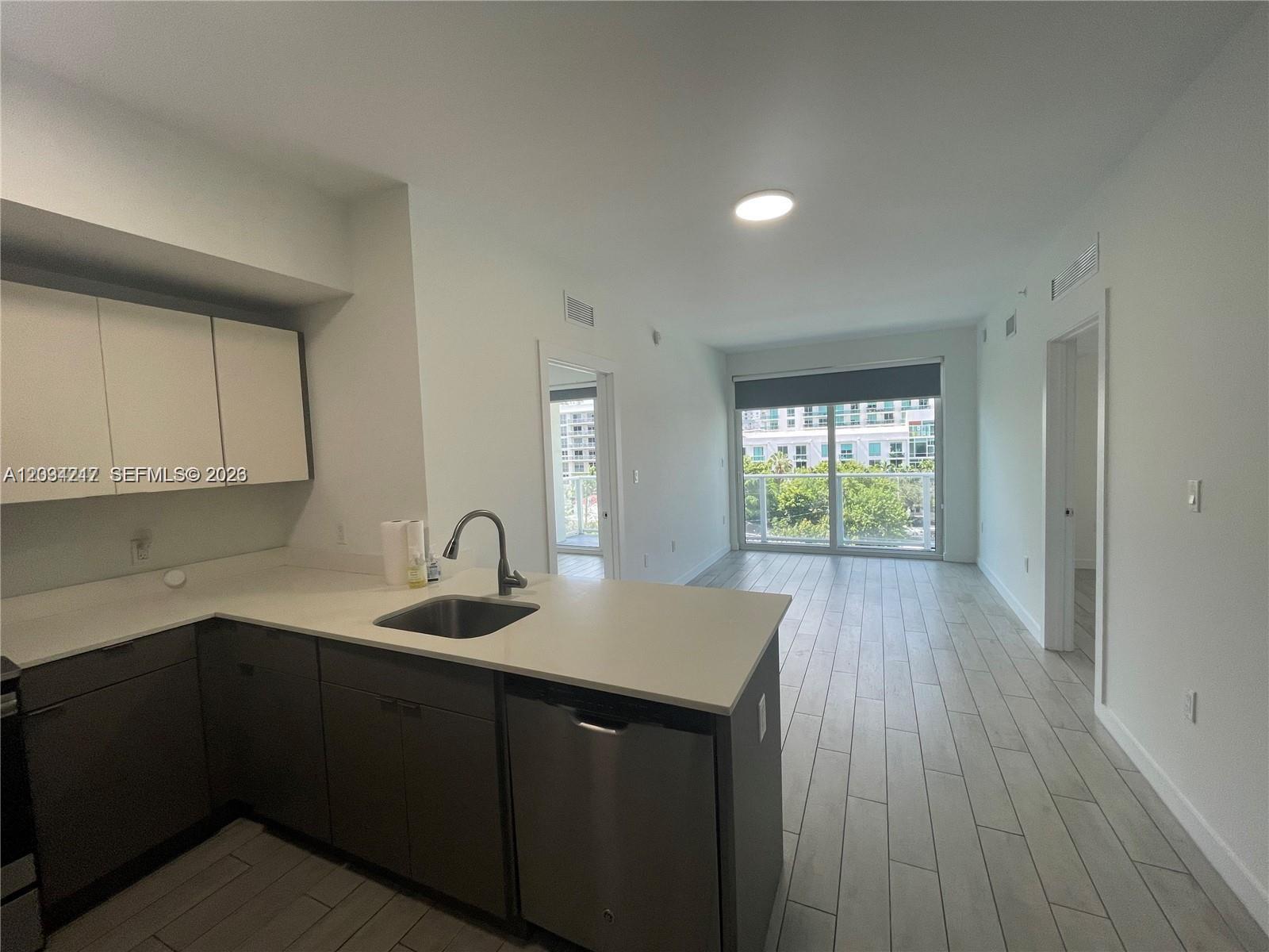 A modern kitchen with dark cabinetry and white countertops opens into a bright living area — 321 NE 26th St # 512, Miami FL 33137, MIAMI, FL