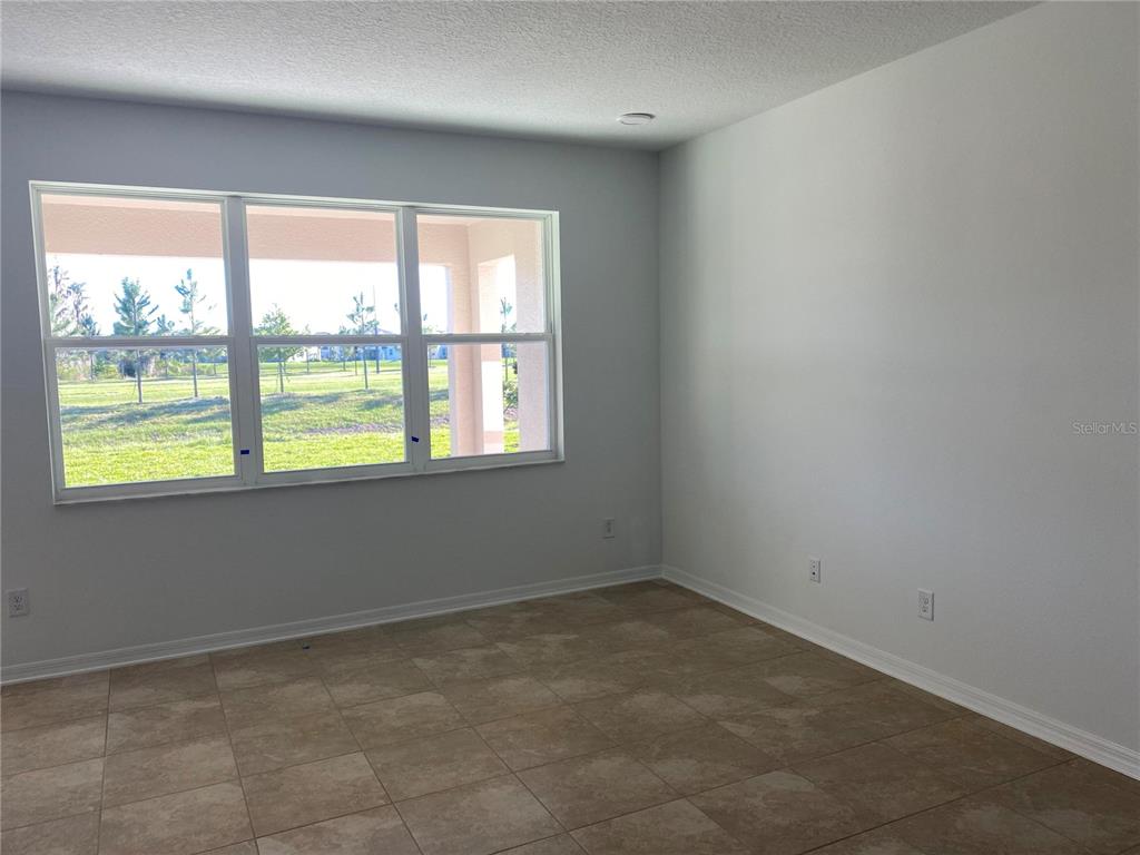 An empty room with light-colored walls, tile flooring, and a large window overlooking a yard — 10725 NEW MORNING DRIVE, TAMPA, FL