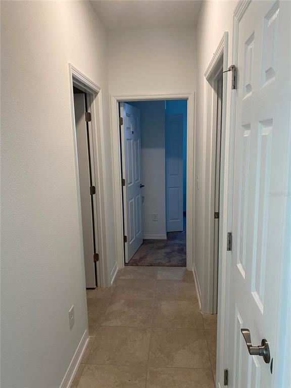 A hallway with tiled flooring leads to an open doorway revealing a carpeted room — 10725 NEW MORNING DRIVE, TAMPA, FL