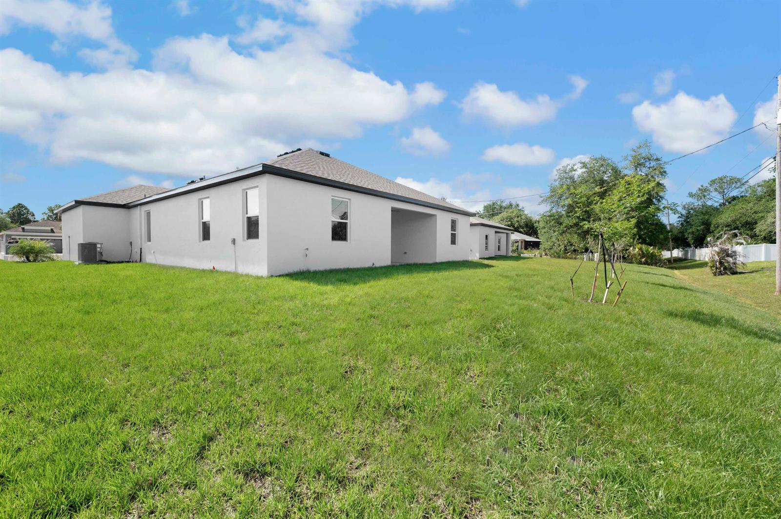 The exterior of a white, single-story house with a large, grassy backyard under a blue sky — 8225 95th Avenue, Vero Beach FL 32967, VERO BEACH, FL