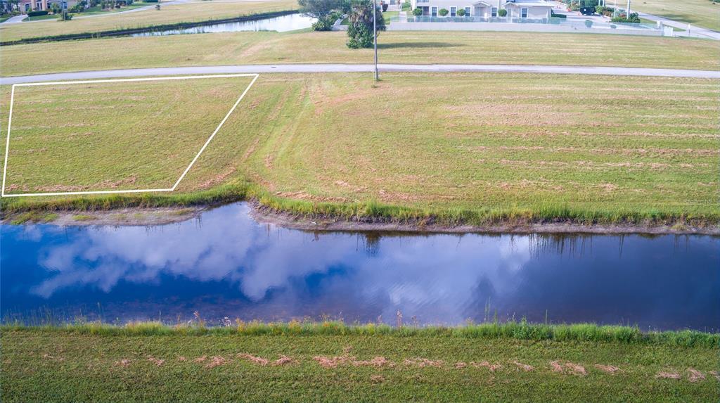 An aerial view shows a vacant grassy lot outlined in white next to a canal — 24060 CHERRYSTONE LANE, PUNTA GORDA, FL