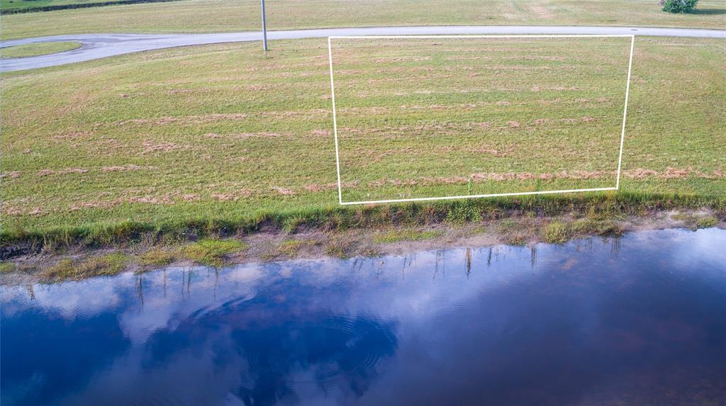 An aerial view shows a grassy lot outlined in white next to a small pond — 24060 CHERRYSTONE LANE, PUNTA GORDA, FL