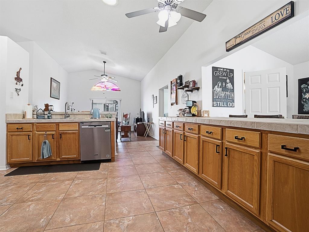 A kitchen features oak cabinets, tile countertops, and tile flooring under a vaulted ceiling — 3851 MANOR OAKS COURT, LEESBURG, FL