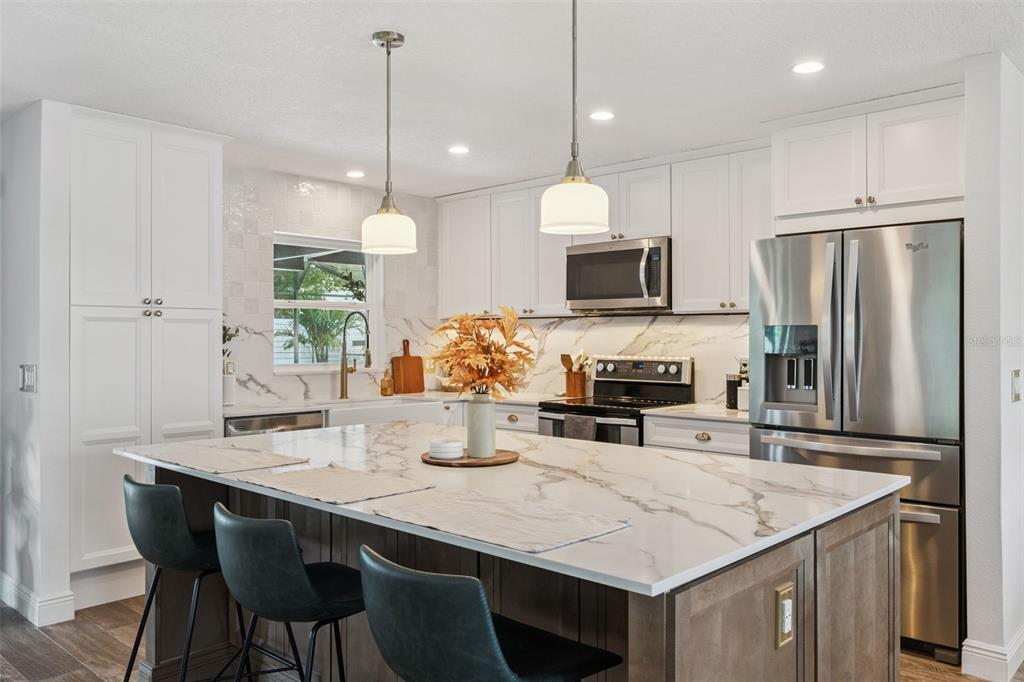 A modern kitchen features a large marble-topped island, white cabinetry, and stainless steel appliances — 8156 CARAWAY DRIVE, ORLANDO, FL