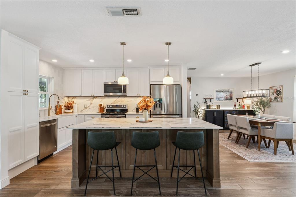 A kitchen features white cabinetry, a marble-topped island with three stools, and an adjacent dining area — 8156 CARAWAY DRIVE, ORLANDO, FL