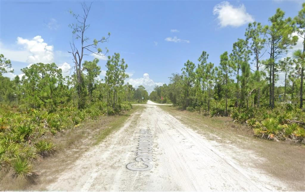 A dirt road stretches through a wooded area toward a distant stop sign — 12285 CARTOUCHE AVENUE, PUNTA GORDA, FL