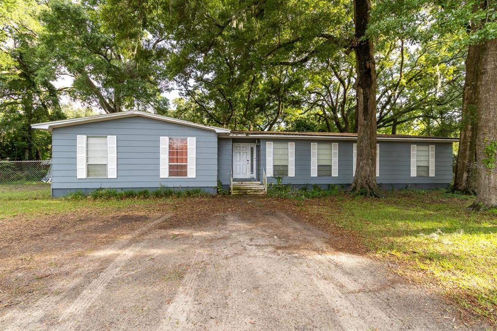 A single-story house with blue siding and white shutters sits behind a dirt driveway — 14215 NW 142ND PLACE, ALACHUA, FL