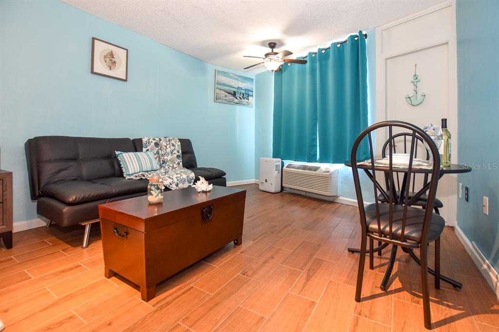 A living room with light blue walls, a black sofa, a wooden trunk, and tile flooring — 313 S. ATLANTIC AVE UNIT 526, DAYTONA BEACH, FL