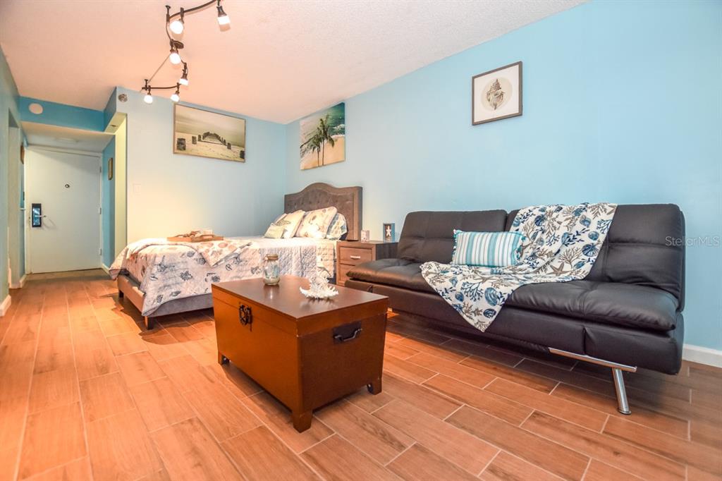 A studio room features a bed, a black sofa, a wooden chest, and light blue walls — 313 S. ATLANTIC AVE UNIT 526, DAYTONA BEACH, FL
