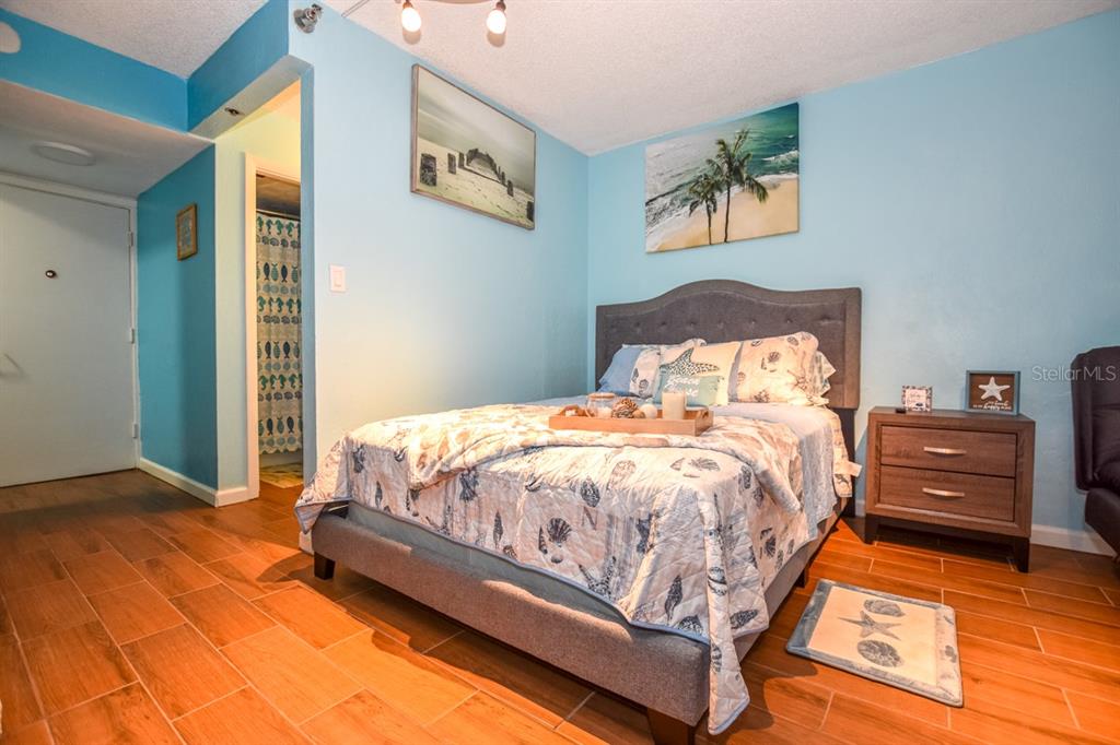 A bedroom features light blue walls, a gray upholstered bed, and wood-look tile flooring — 313 S. ATLANTIC AVE UNIT 526, DAYTONA BEACH, FL