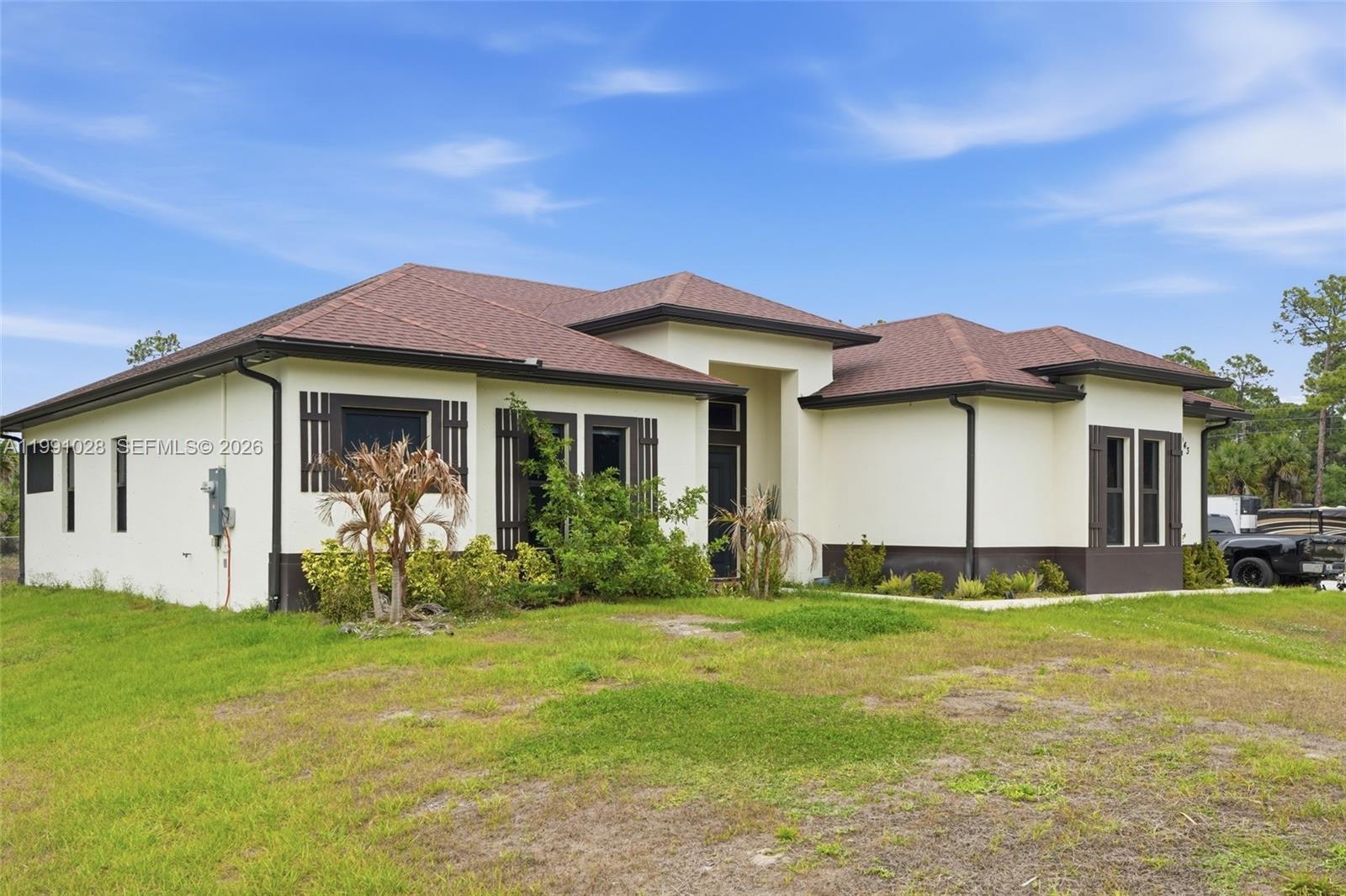 A single-story house with a white stucco exterior, brown roof, and dark window shutters — 3043 18, Naples FL 34120, NAPLES, FL