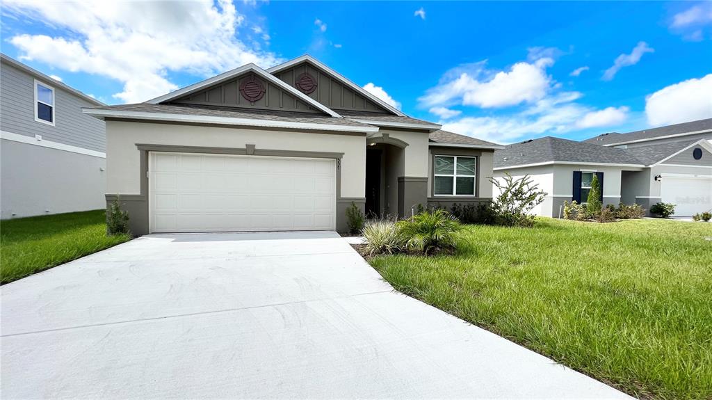 A beige single-story house features a two-car garage, a concrete driveway, and a grassy lawn — 557 SCOTT LAKE CREEK LN, LAKELAND, FL