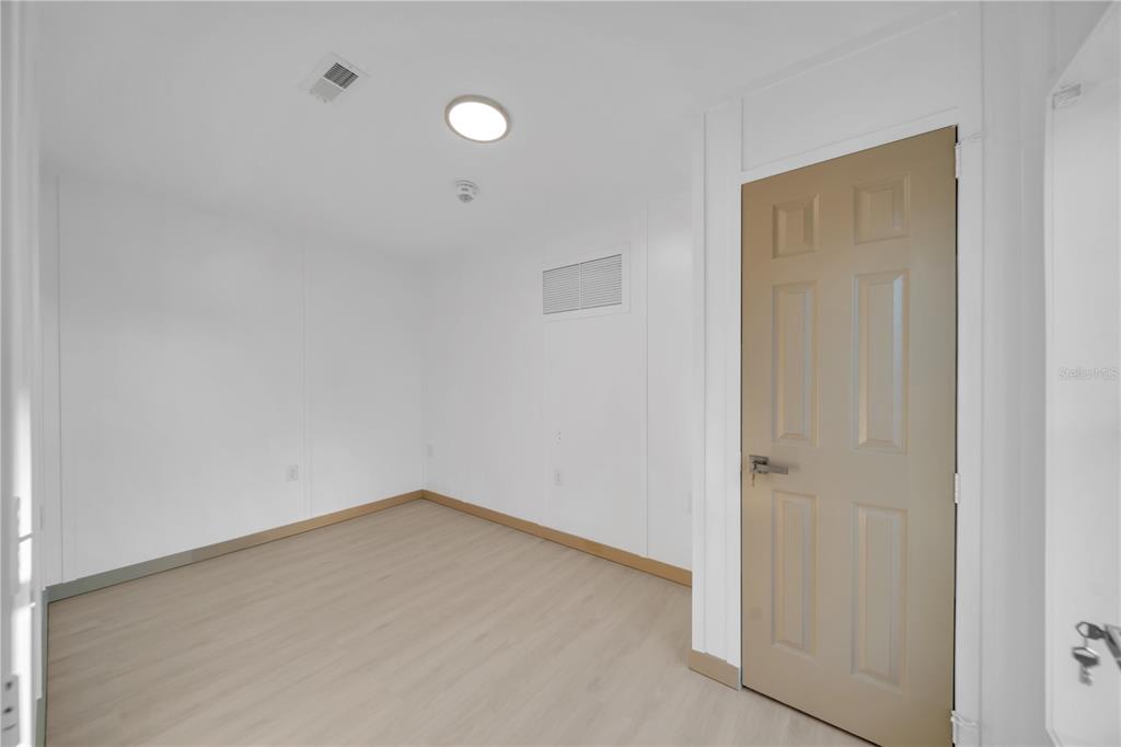 An empty room with white walls, light wood-look flooring, and a tan interior door — 7483 DANVERS CIRCLE, PORT CHARLOTTE, FL