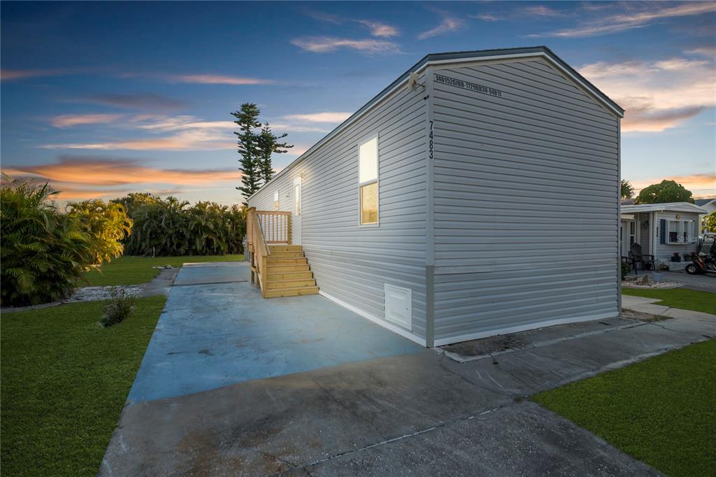 A light gray mobile home with a wooden staircase sits on a concrete driveway at sunset — 7483 DANVERS CIRCLE, PORT CHARLOTTE, FL