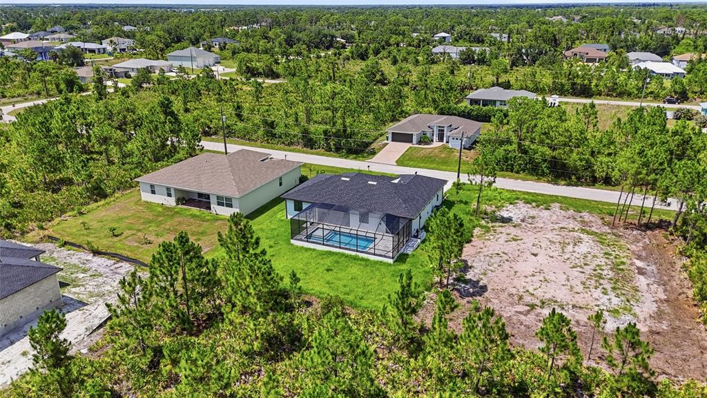 An aerial view shows two suburban houses with swimming pools surrounded by dense pine forest — 14041 NEWSON LANE, PORT CHARLOTTE, FL
